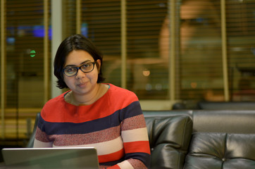 Young confident professional working woman on a laptop in airport lounge during transit/layover. Outline of an aeroplane is visible in the background from the window 