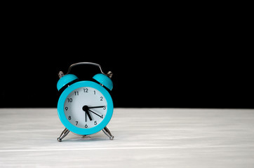 Blue retro alarm clock on a black and white wooden background, with a copyspace, a concept of the morning, a countdown