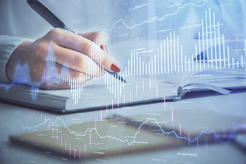 Multi exposure of woman's hands making notes with forex graph hologram. Concept stock market...