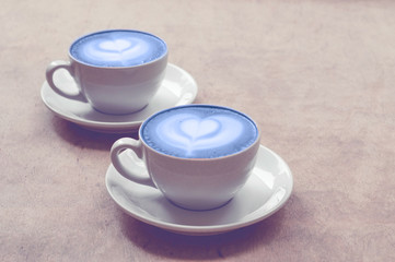 Two cup of cappuccino with blue latte art on wooden background. Hot coffee on table. Top view, flat lay copy space for text. Copy space. Trend tonning