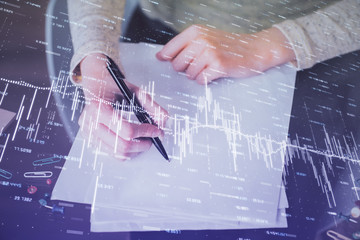 Hand taking notes in notepad. Forex chart holograms in front. Concept of research. Multi exposure