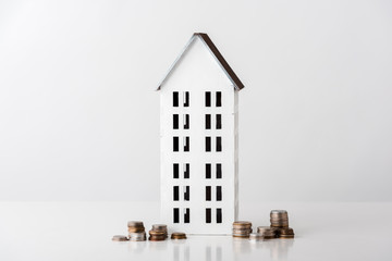 carton house near stacks with golden and silver coins on white