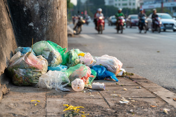 Pile of garbage bags and messy trash on street sidewalk with traffic on background in Hanoi, Vietnam