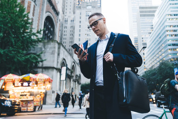 Young handsome businessman checking app on phone on busy street