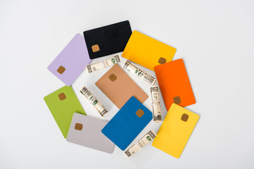 top view of multicolored credit card templates near cash rolls isolated on white
