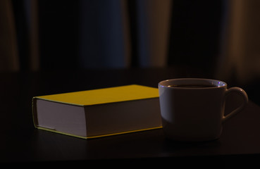 A yellow book on a black living room table with a cup of black filter coffee