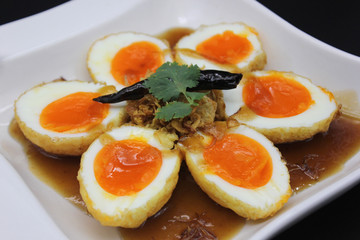Close-up Fired hard boiled eggs in tamarind sauce topping with fired shallots and dry chili or in Thai call Kai Look Keuy in the white plate.