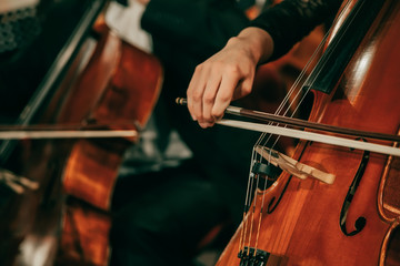 Symphony orchestra on stage, hands playing cello. Shallow depth of field, vintage style. - obrazy, fototapety, plakaty