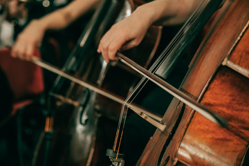 Symphony orchestra on stage, hands playing cello. Shallow depth of field, vintage style.