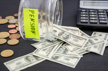 Fototapeta premium jar with the inscription PENSION, dollars, calculator and coins on a wooden table