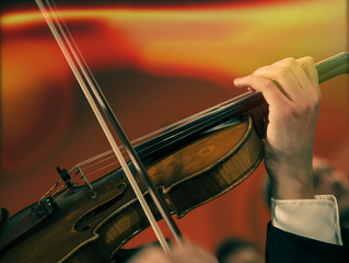 Symphony orchestra on stage, hands playing violin. Shallow depth of field, vintage style.