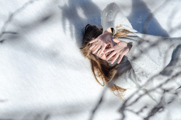 young blonde girl with glasses lying on top of snow and covering her face with her hands