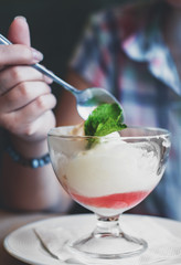 young girl's hand holding a spoon and eating ice cream in glass at a table in cafe