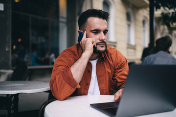 Male freelancer talking on smartphone sitting in cafe