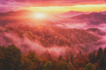 Fototapeta na wymiar Amazing nature landscape, misty colorful sunrise in Alps, scenic view of wooded mountains with autumn trees, dramatic cloudy sky and rising sun. Outdoor travel background, Jamnik, Slovenia