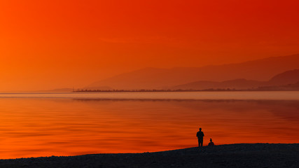 Fototapeta na wymiar Seascape with orange sunset and silhouettes of people.