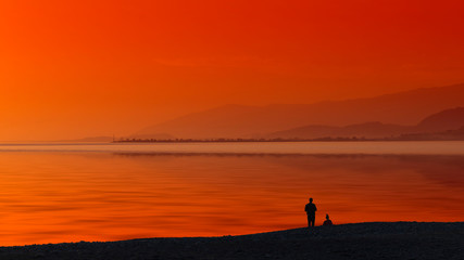 Fototapeta premium Seascape with orange sunset and silhouettes of people.