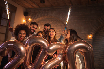People at New Year party, waving with sparklers and holding 2020 balloons