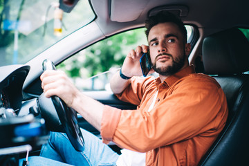Man in casual clothing driving car and speaking on smartphone while looking away
