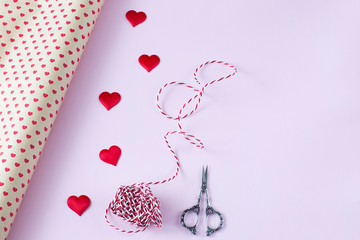 gift wrapping paper, scissors, ribbon and satin hearts on a pink background