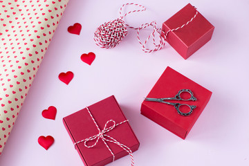 gift wrapping paper, scissors, ribbon, three red gift boxes and satin hearts on a pink background