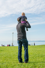 Rear view of a father holding his cute baby daughter and looking the sea.