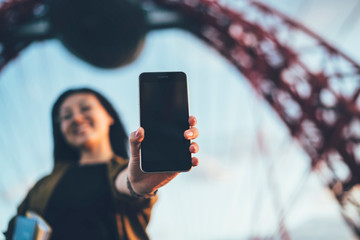 Selective focus on modern digital smartphone device with advertising copy space area, woman holding mobile phone standing on blurred background outdoors showing new application or content on screen
