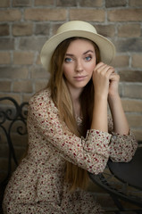 Close-up portrait of a tender young girl in an elegant hat at a table in a cafe