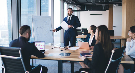 Happy employee presenting scheme on whiteboard to executives