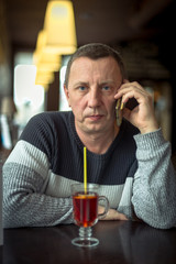 A serious man in a sweater talking on a mobile phone in a cozy cafe. Solving issues over a Cup of tea. Concept of modern technologies and mobile communication
