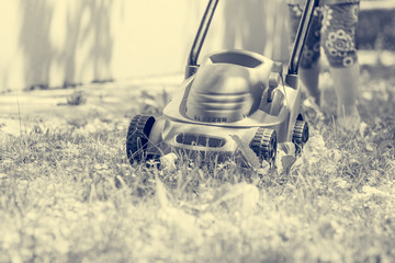 Deatil of plastic toy lwn mower with child pushing it. - obrazy, fototapety, plakaty
