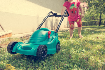Cute girl lawn mowing with plastic toy mower. - obrazy, fototapety, plakaty