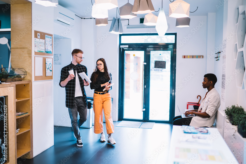 Aufkleber young classmates walking to university lecture in campus hallway and discussing project information 