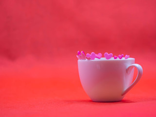 Closeup of white coffee cup and pink paper sticker on vivid or vibrant red background for love, valentine, romance, wedding, greeting card concept and idea.