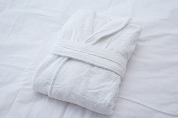 Clean folded bathrobe on white bed. - obrazy, fototapety, plakaty