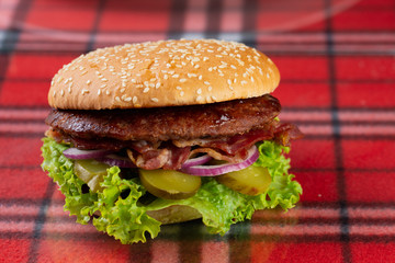  pork burger with cheese, tomatoes, cucumber, onions. bun with sesame seeds and bacon