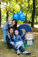 Family life. Portrait of parents and their children in the Park. Birthday of a two year old boy. Decor with the number two with lion and balloons.