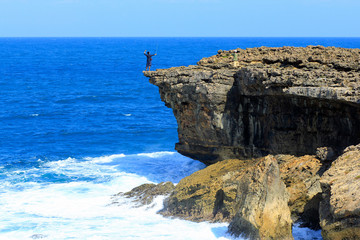 Fototapeta na wymiar Yogyakarta, Indonesia, June 12, 2015. A tourist endangers his life by taking a selfie at the edge of a cliff at Timang Beach.