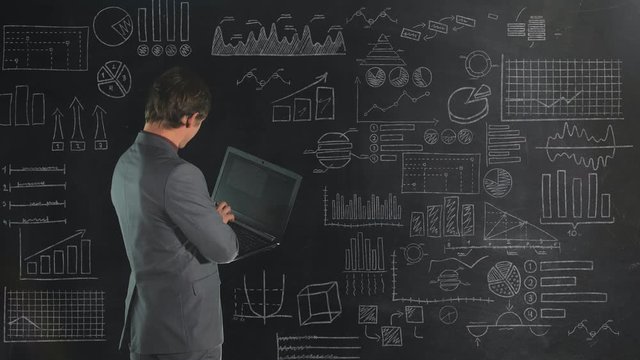 A man in front of a chalk board analyzes data from an infographic.