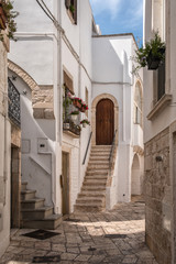 Fototapeta na wymiar Narrow deserted street, stairs and white houses. Locorotondo, Italy.
