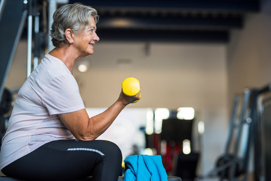 mature woman at the gym training her body and her biceps sitting in a bench with a dumbbell in her hand - healthy and fitness senior lifestyle