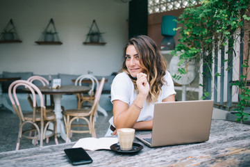 Fototapeta na wymiar Pensive smiling woman sitting in cafe with laptop