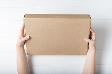 Rectangular cardboard box in children's hands. Top view, white background