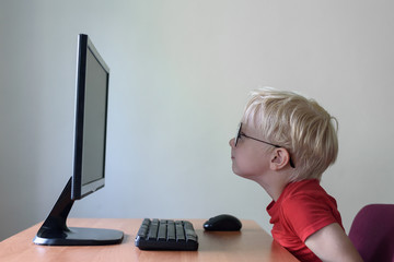 Blond boy with glasses sits his nose buried in a monitor. Internet and preschooler