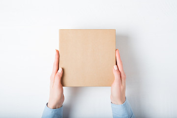 Square cardboard box in female hands. Top view, white background