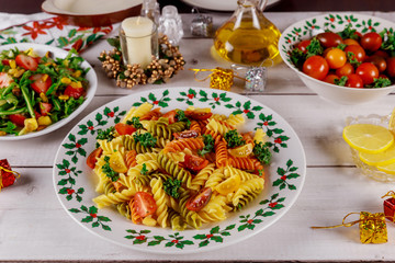 Festive christmas dinner with colorful pasta, cherry tomatoes, salad on white wooden table.