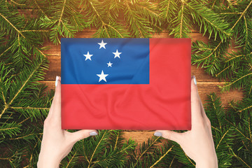 Box with Samoa flag in female hands. Fir branches on the background