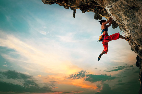 Athletic Woman climbing on overhanging cliff rock with sunset sky background.
