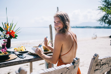 Young woman traveler sitting at table and eating on seaside