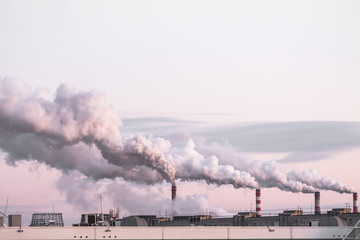 industrial chimneys with heavy smoke causing air pollution as ecological problem on the pink sunset...